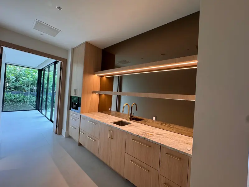 White oak wet bar with floating lit shelves and a stone counter by Eco Woodwork & Design