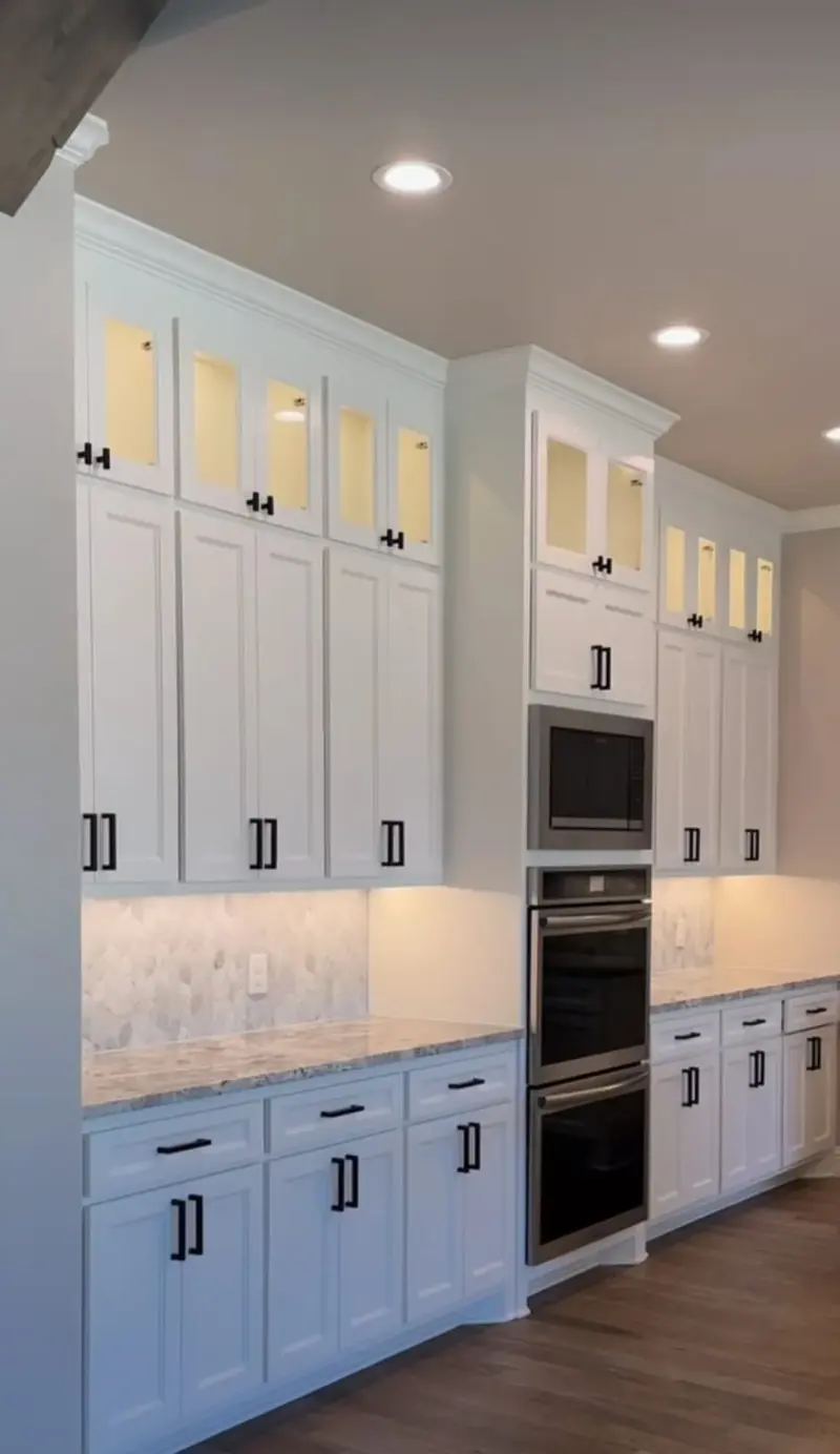 Tall white kitchen cabinetry with glass-front uppers and built-in ovens