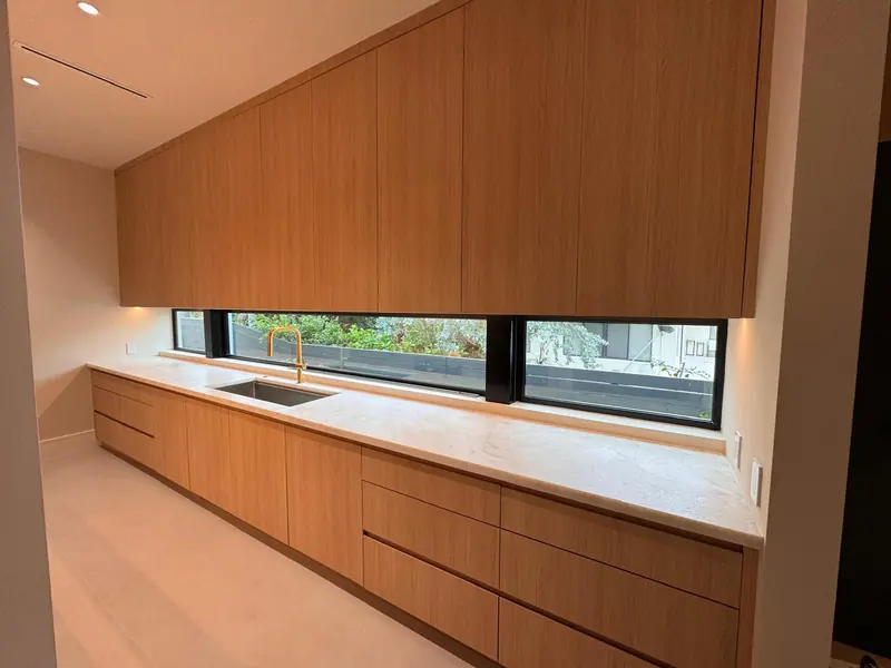 White oak kitchen wall with flat-panel cabinetry and a stone countertop under the window by Eco Woodwork & Design