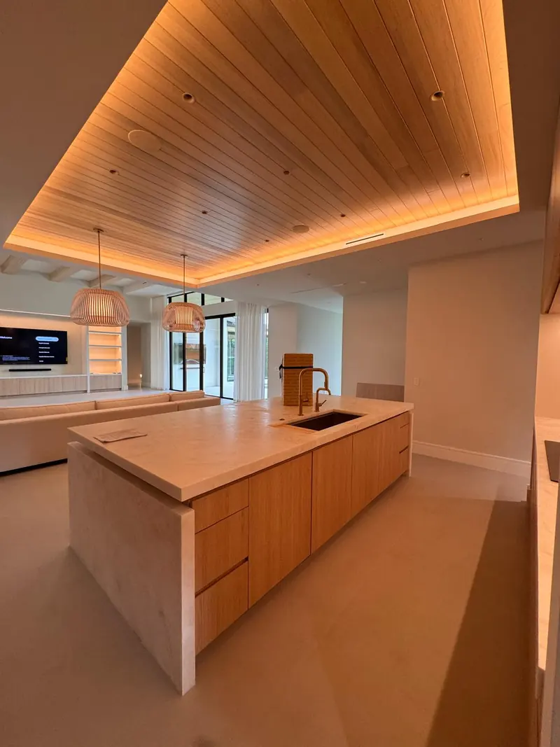 White oak kitchen island under a lit wood-slat ceiling by Eco Woodwork & Design