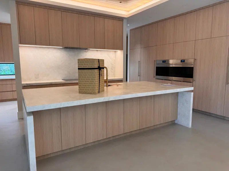 White oak kitchen island with a waterfall stone top and full-height cabinetry by Eco Woodwork & Design